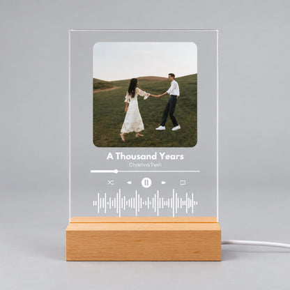 Studio front view of unlit clear acrylic plaque featuring custom couple photo, song title, artist, and sound wave on a wooden base.