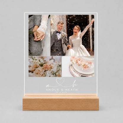 Studio front view of unlit clear acrylic plaque printed with a 4-photo wedding collage, monogram initials heart line, couple names, and date on a natural beech wood base.