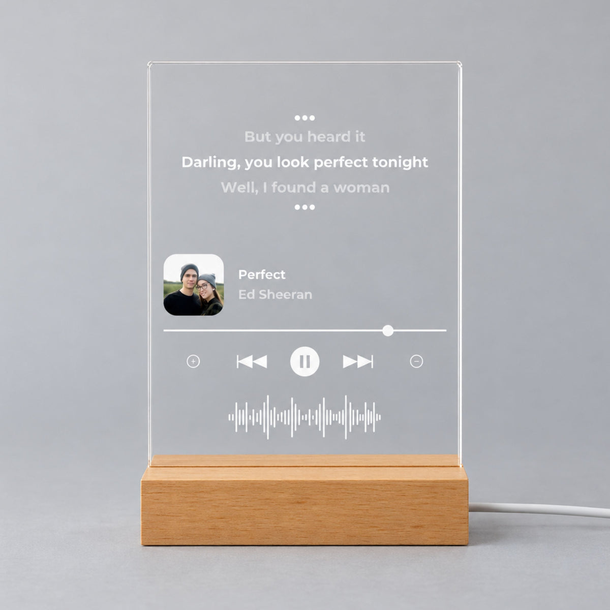 Studio front view of unlit clear acrylic plaque printed with favorite song lyrics, small square photo, song details, and sound wave on a wooden base.