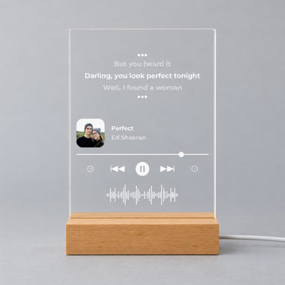 Studio front view of unlit clear acrylic plaque printed with favorite song lyrics, small square photo, song details, and sound wave on a wooden base.
