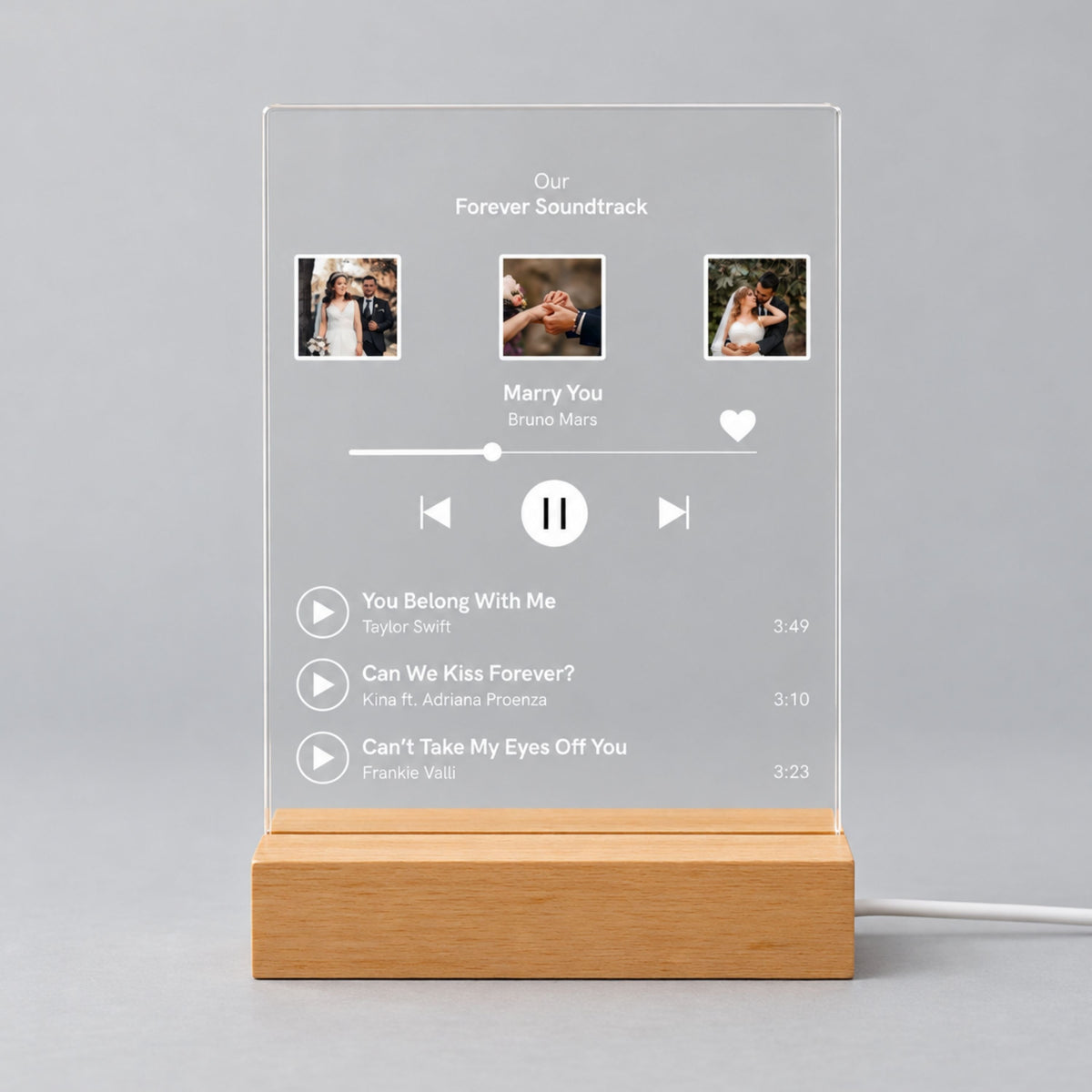 Studio front view of unlit clear acrylic plaque printed with 3 wedding photos, custom playlist title, featured song, and track list on a wooden base.