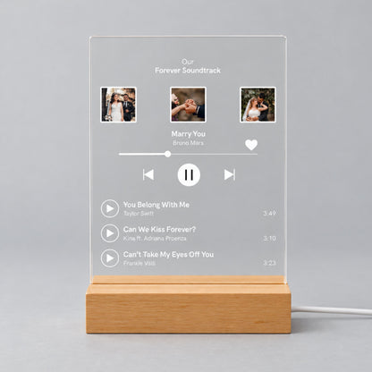 Studio front view of unlit clear acrylic plaque printed with 3 wedding photos, custom playlist title, featured song, and track list on a wooden base.