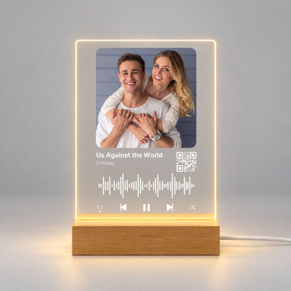 Studio front view of illuminated custom music acrylic night light with photo and scannable QR code glowing warm white on a natural wooden LED stand.