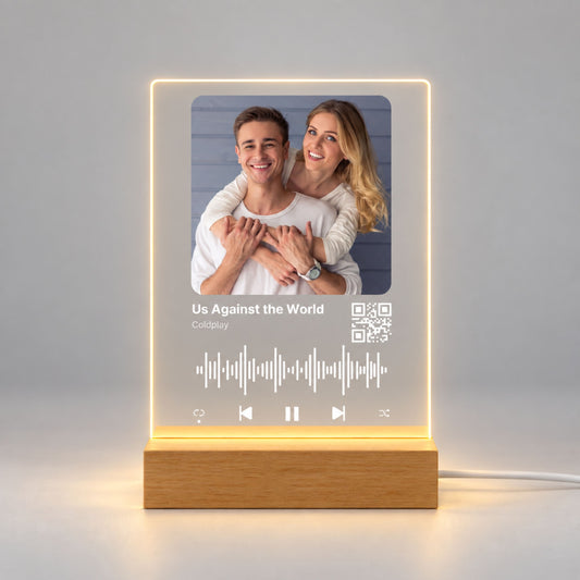 Studio front view of illuminated custom music acrylic night light with photo and scannable QR code glowing warm white on a natural wooden LED stand.