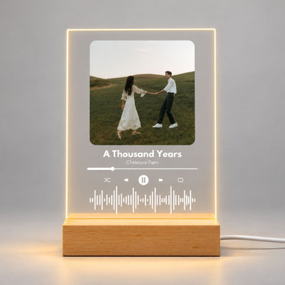 Studio front view of illuminated custom music acrylic night light with couple photo and sound wave glowing warm white on a wooden LED stand.