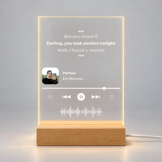 Studio front view of illuminated acrylic night light featuring custom song lyrics and small photo glowing warm white on a natural wooden LED stand.