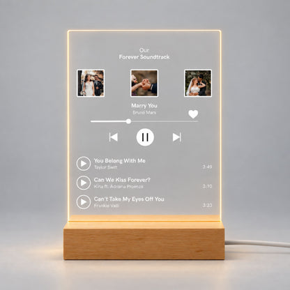 Studio front view of illuminated custom music playlist acrylic plaque with 3 wedding photos and song list glowing warm white on a wooden LED stand.