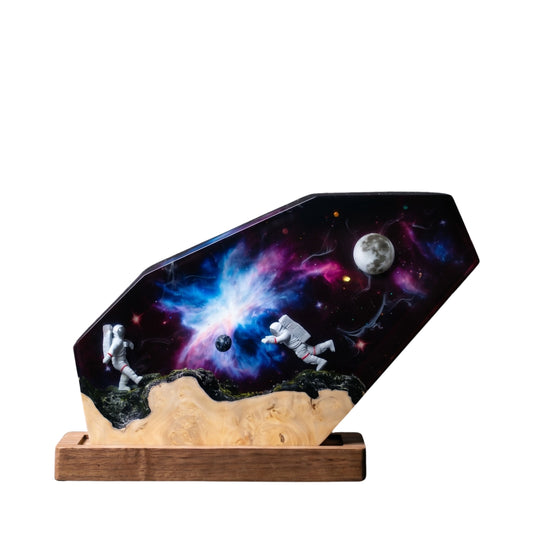 Handcrafted space nebula epoxy resin night light on a wooden base isolated on a white background, featuring a vibrant purple and blue galaxy scene with two miniature astronauts exploring near a detailed moon and distant stars.
