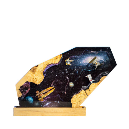 Handcrafted space exploration epoxy resin night light on a wooden base isolated on a white background, featuring miniature spaceships, a satellite station, and an astronaut floating through a dark starry cosmos with detailed planets and a glowing dust nebula.