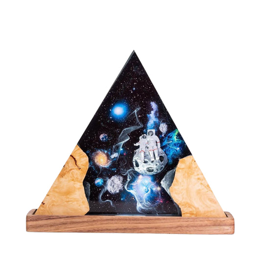 High-resolution studio shot of a triangular epoxy resin lamp on a wooden base, featuring a miniature explorer figure amidst blue and black cosmic swirl patterns on a white background.