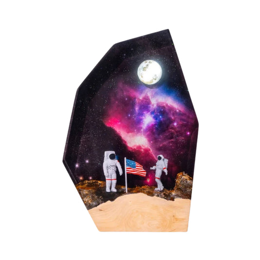 A geometric handmade resin and wood lamp featuring two miniature astronauts planting an American flag on a rocky moon surface, set against a deep space backdrop with a bright moon and colorful nebula.