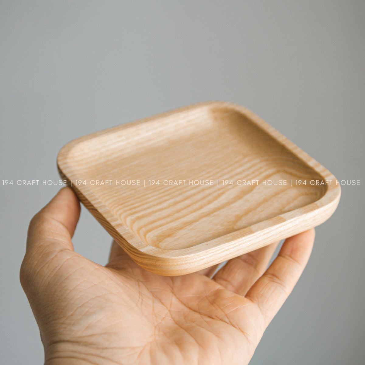 Light wood square tray with raised edges shown resting in a person's open hand
