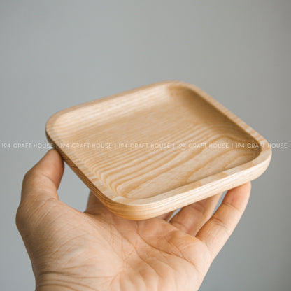 Light wood square tray with raised edges shown resting in a person's open hand