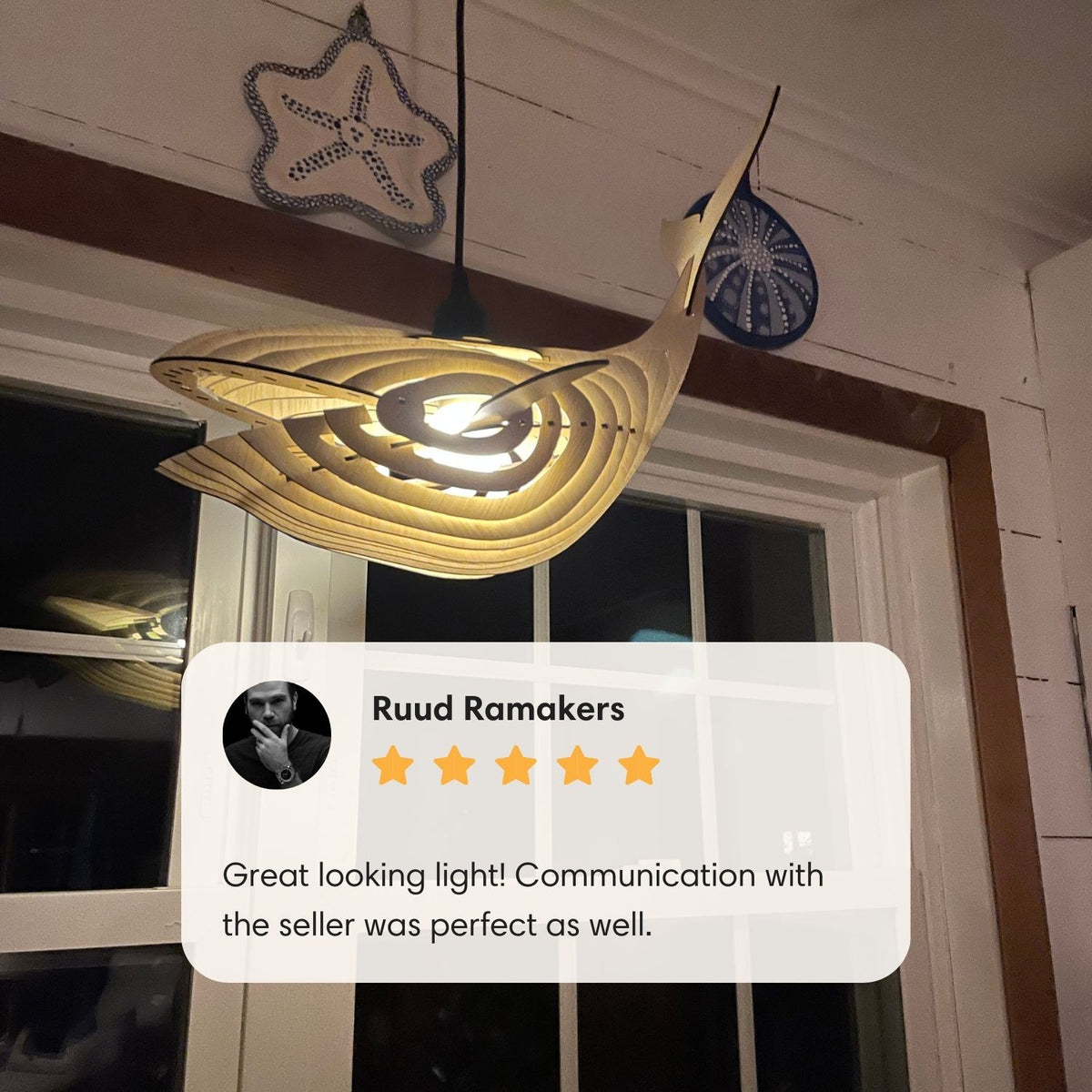 Illuminated whale pendant light hanging by a window with customer review overlay