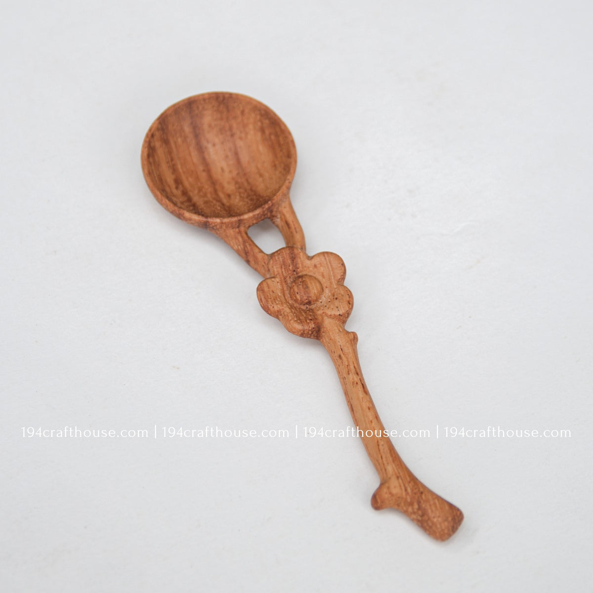 Angled view of a handcrafted Doussie wood spice spoon with a carved flower handle and round mini scoop.