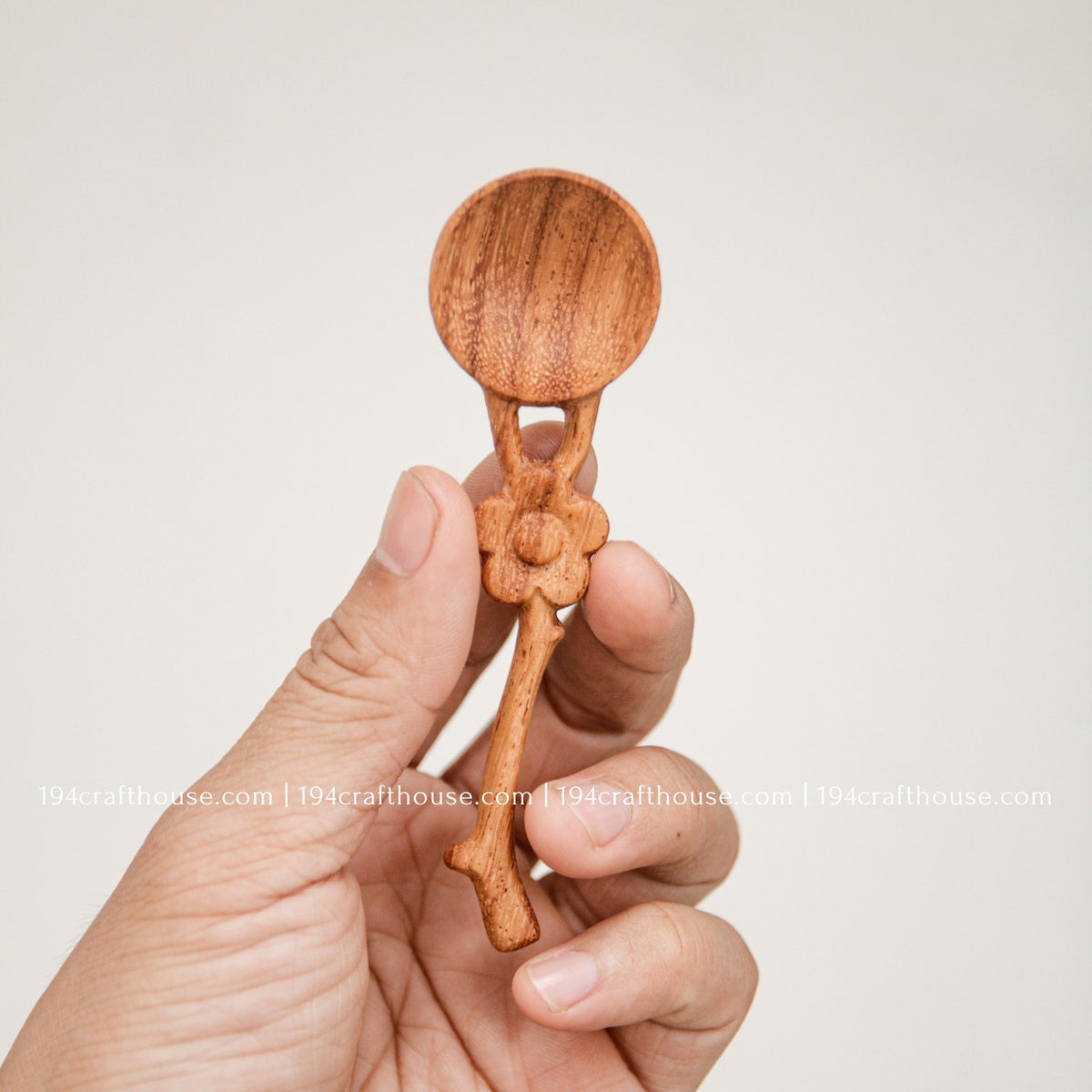 Hand-held Doussie wood spice spoon with flower-shaped handle, showing its small measuring scoop size and natural finish.