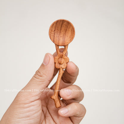 Hand-held Doussie wood spice spoon with flower-shaped handle, showing its small measuring scoop size and natural finish.
