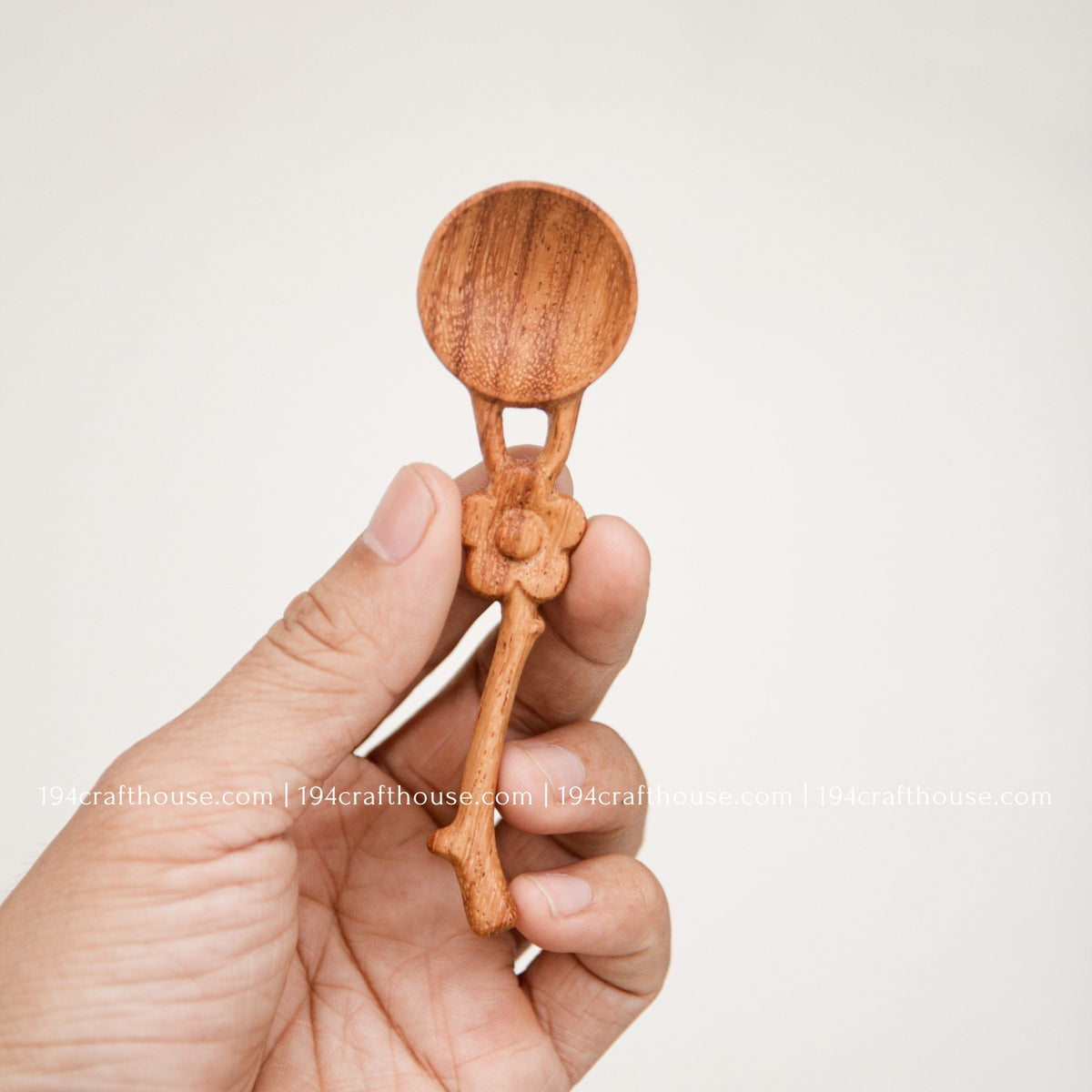 Flower handle wooden spice spoon held in hand to show the compact size, carved detail and natural wood grain.