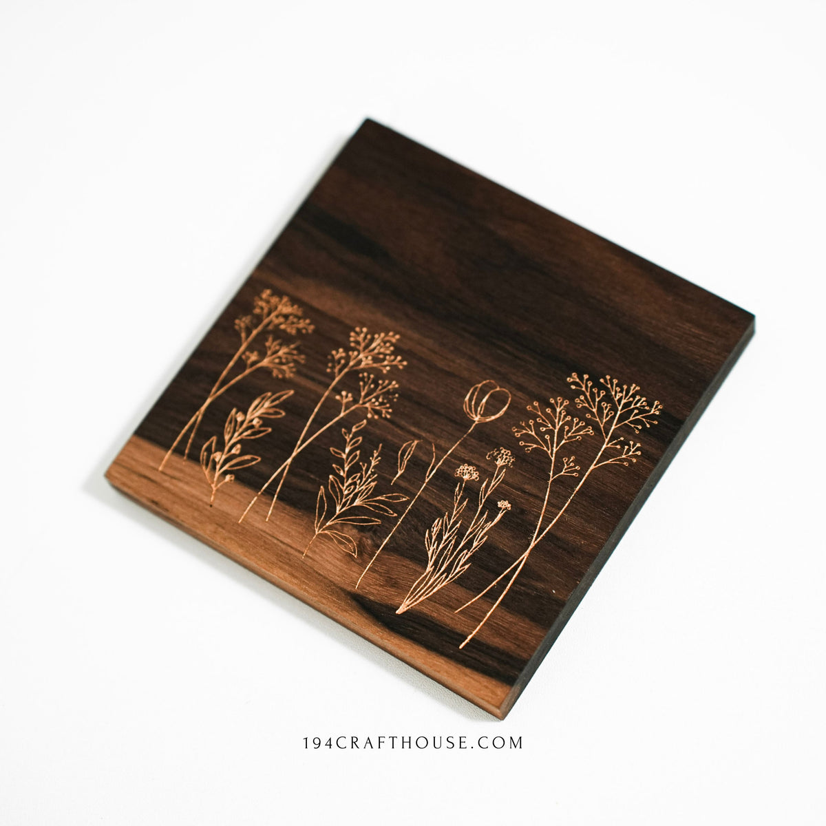 A walnut wood coaster with engraved wildflowers shown at an angle on a white background.
