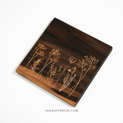 A walnut wood coaster with engraved wildflowers shown at an angle on a white background.