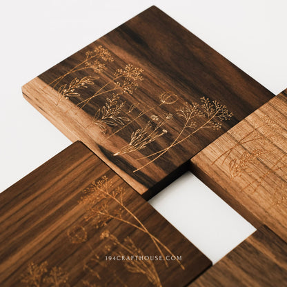 Close-up of walnut coasters showing engraved wildflower botanical designs and wood grain details.