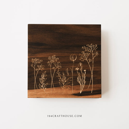 Square walnut wood coaster with engraved wildflower design photographed flat on a white background.