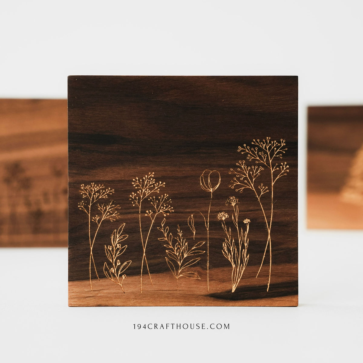 Front view of a walnut wood coaster with engraved wildflower design, with other coasters blurred behind.