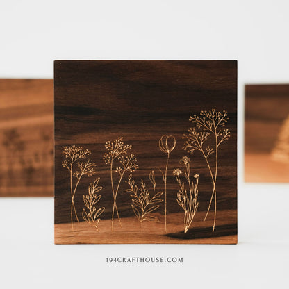 Front view of a walnut wood coaster with engraved wildflower design, with other coasters blurred behind.