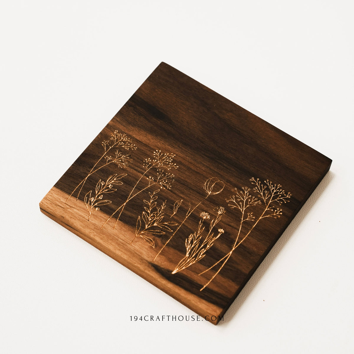 Walnut wood coaster with wildflower engraving shown from a side angle on a white surface.