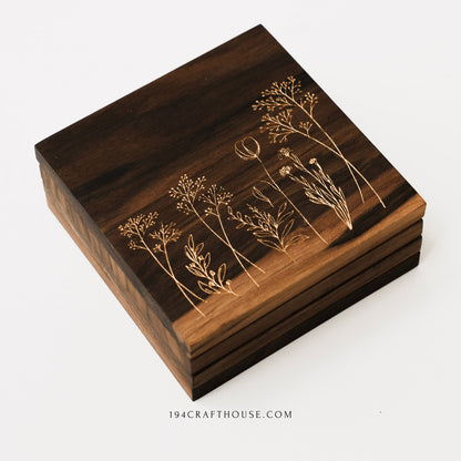 Angled view of a stack of walnut wood coasters featuring engraved wildflower designs on the top piece.