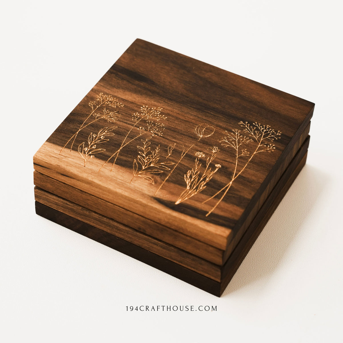 Side view of stacked walnut coasters with engraved wildflower botanical design visible on the top coaster.