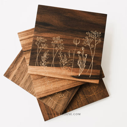 Four walnut wood coasters with engraved wildflower designs stacked in a fan shape on a white background.